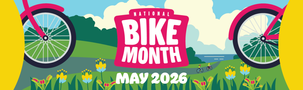Pink Bike Month logo set in a scene of rolling hills with a paved trail lined with flowers. A bike wheel is on either side of the logo. It reads 